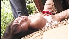 Tied Asian girl lying half naked on the bare ground